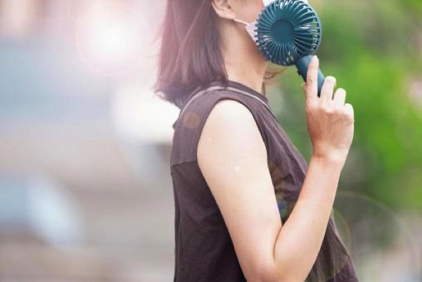 小型扇風機で体を冷やす女性