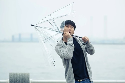 強風で傘を持っていかれる男性