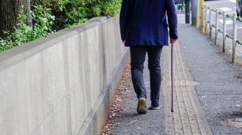 杖をつき歩道を歩く高齢者