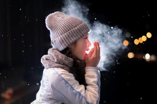 寒さで手に息を吐く女性